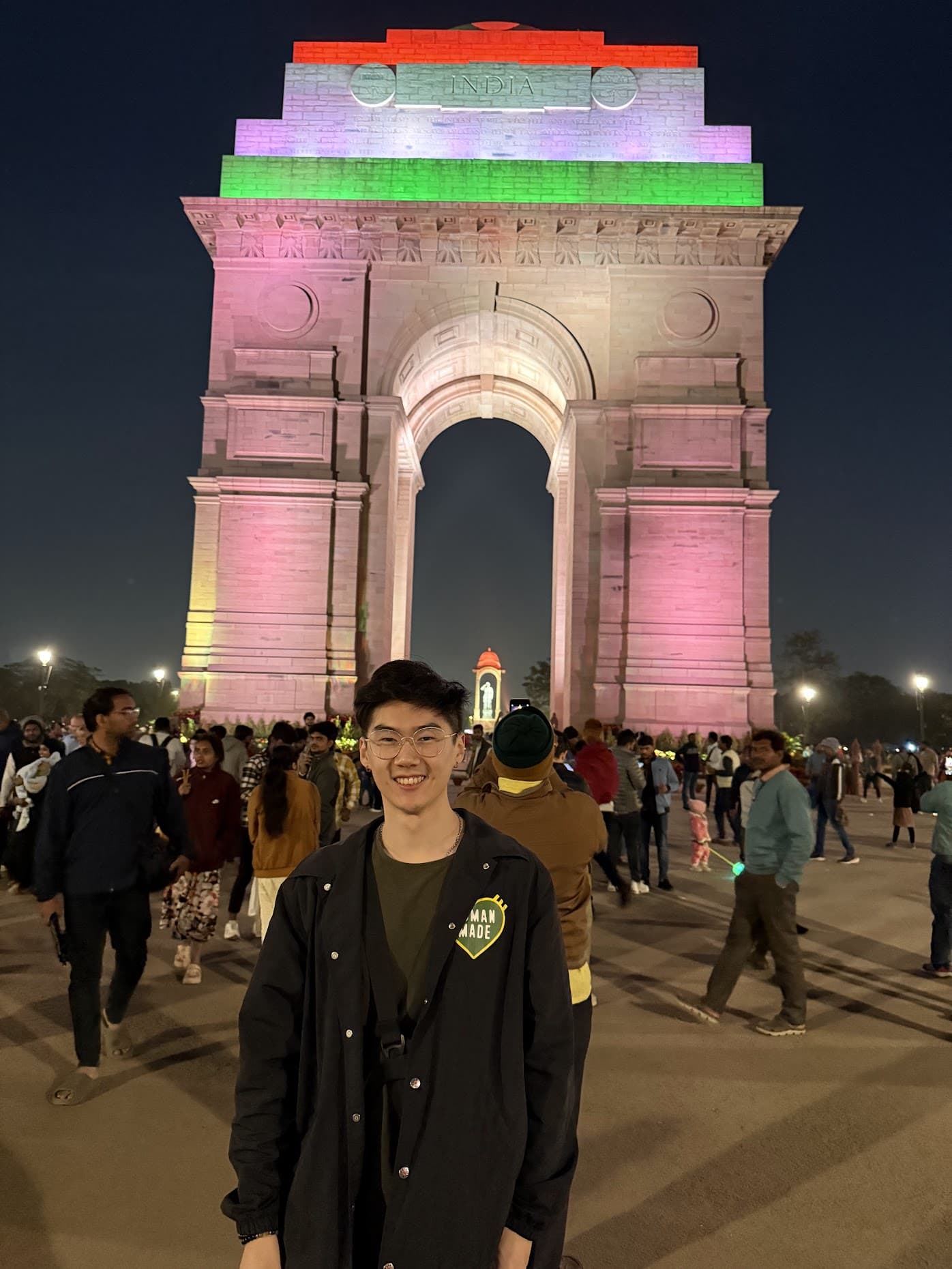 India Gate at night, lit up in the orange, white, and green of the Indian flag, with crowds gathered below