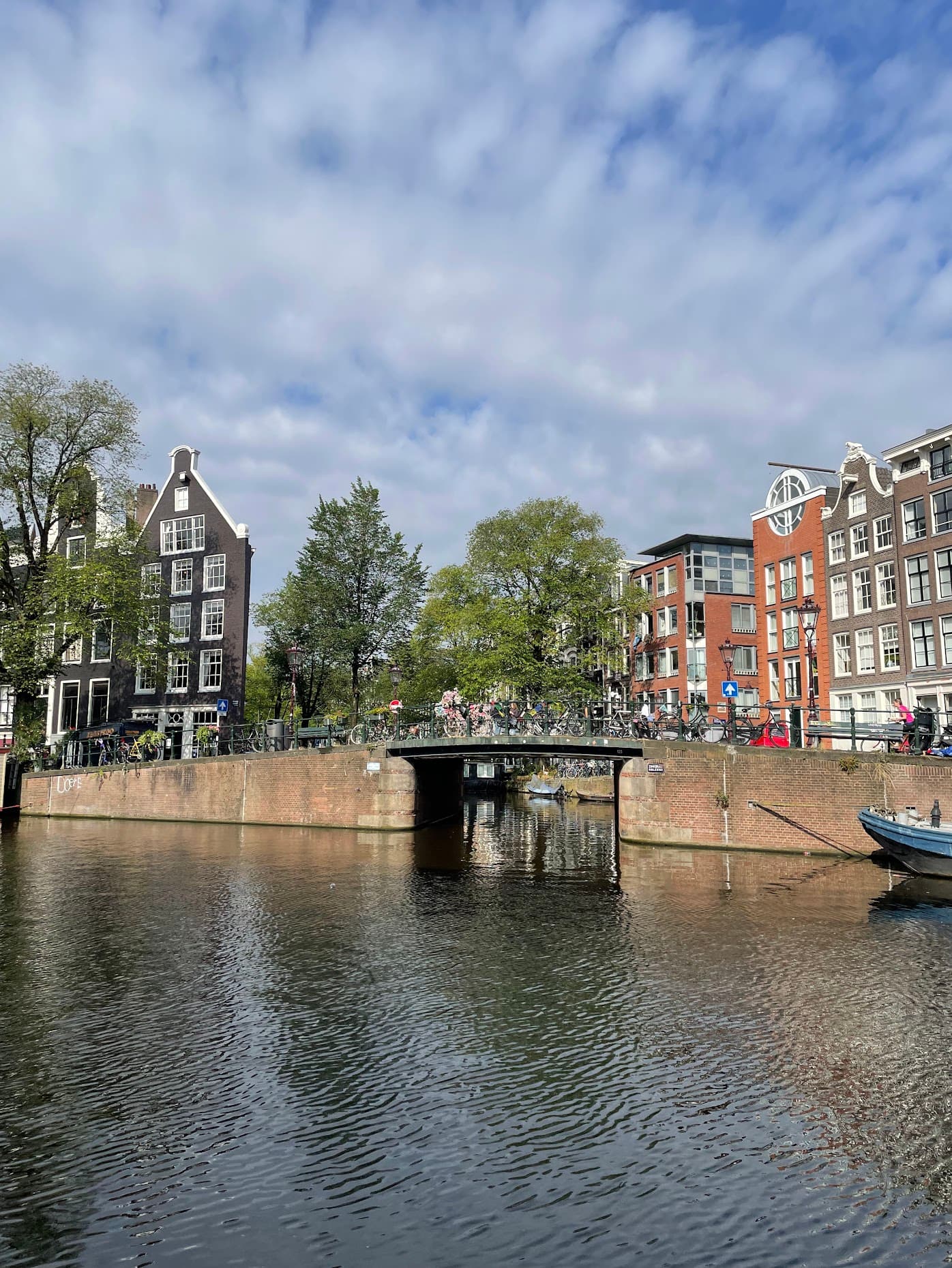 A bike-lined bridge crossing an Amsterdam canal with crooked canal houses on both sides