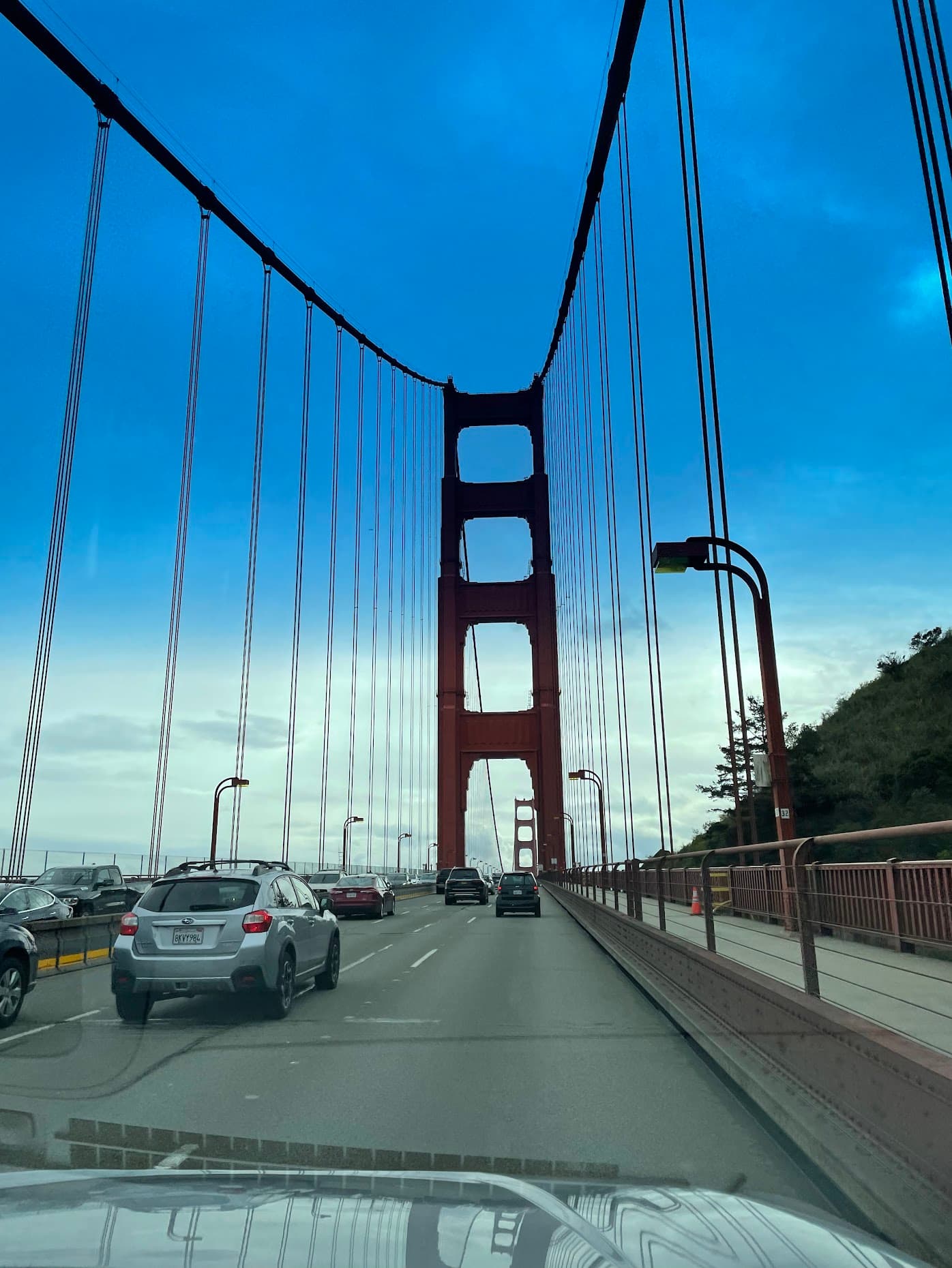 Looking up at a red tower of the Golden Gate Bridge mid-crossing, suspension cables fanning overhead