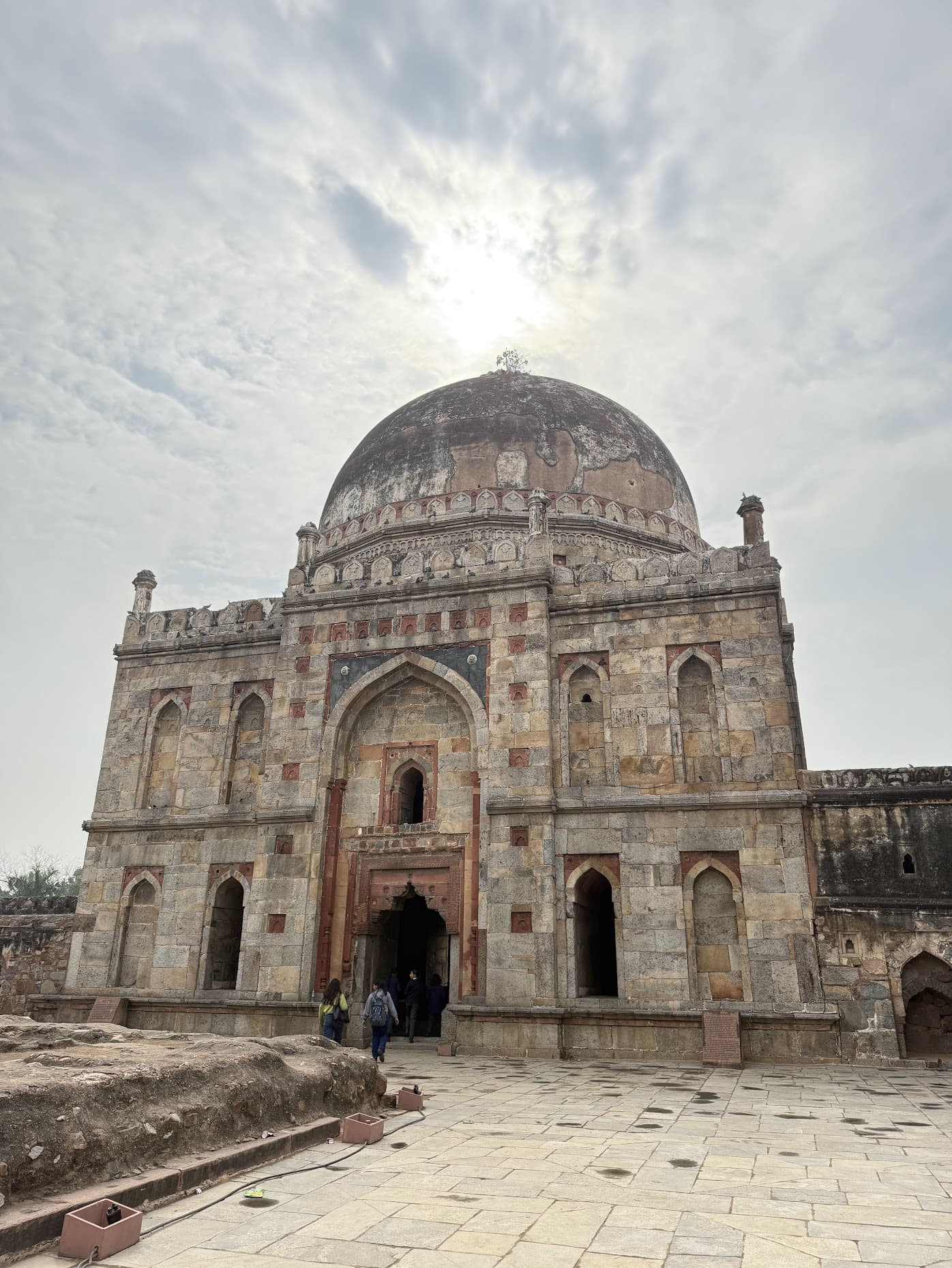 A domed 15th-century tomb rising over the stone plaza in Lodi Gardens, Delhi, with the sun behind it